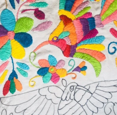 Close-up of Tenango embroidery showing colorful birds and flowers hand-stitched on natural fabric