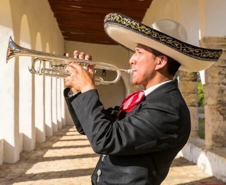 Mariachi trumpet player in traditional charro suit and embroidered sombrero performing in a sunlit colonial corridor in Mexico.